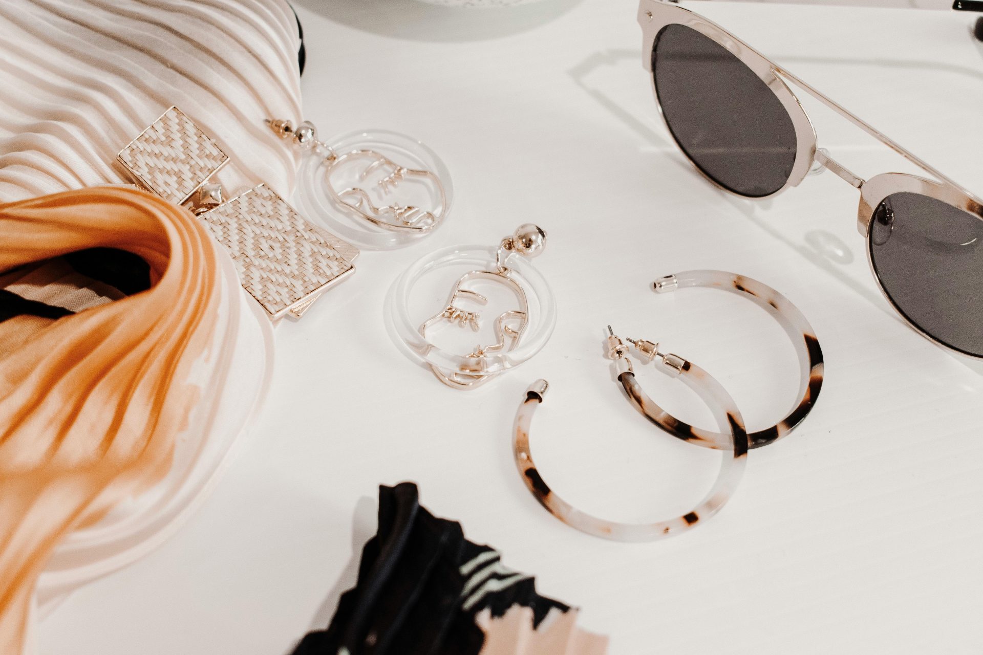 Stylisches Flat Lay moderner Modeaccessoires, darunter Ohrringe, ein Schal und eine Sonnenbrille.